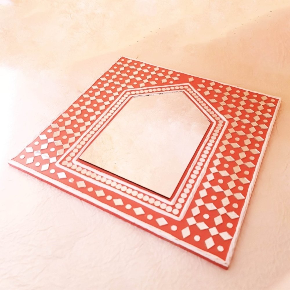 Bright brick red handcrafted mud art mirror, adding warmth and character