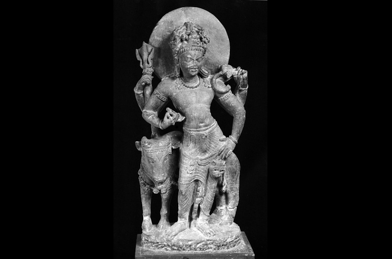 A beautiful schist stone image of a four-armed (Chaturbhuja) standing Shiva leaning on Nandi