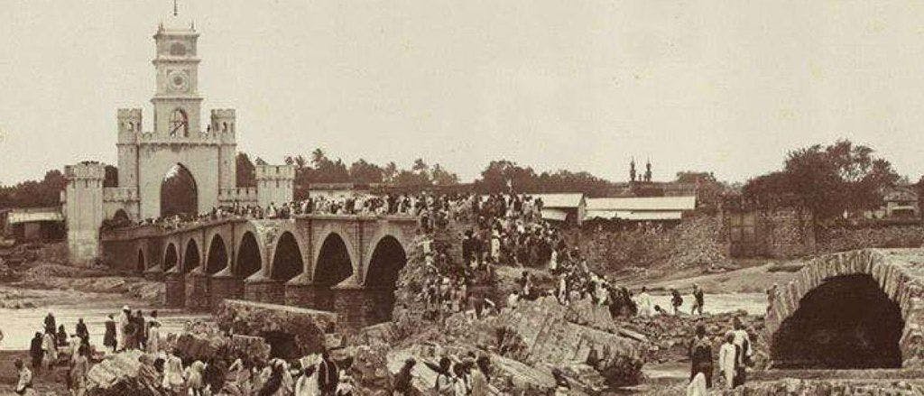Survivors walk across a bridge with the Afzal Darwaza in the background